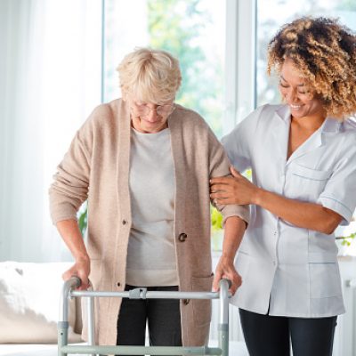 Cheerful friendly nurse helping senior woman to use walking frame